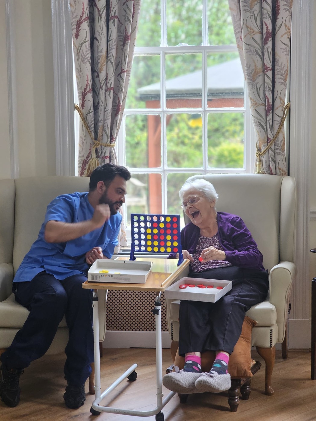 A carer and resident sharing a game of Connect 4 at Woodside View